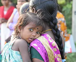 A child resting her head on her mother's shoulder, looking at the camera