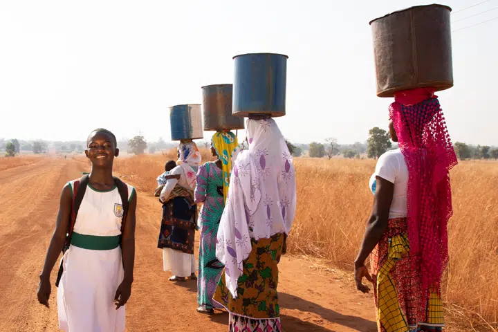 Women standing in desert with tub on their head and a girl with bagpack