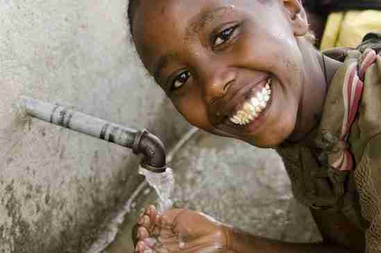 A young girl smiling and catching fresh water in her hands from a running tap