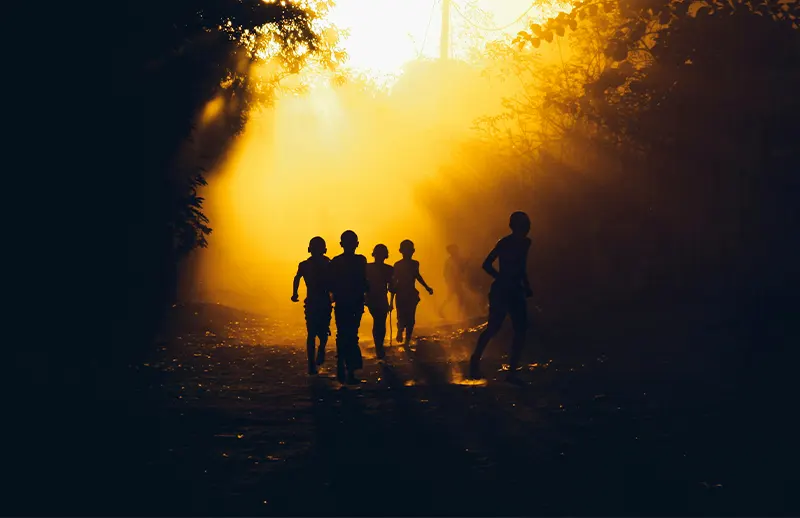 Children running in the sunset, only their silhouettes are visible.