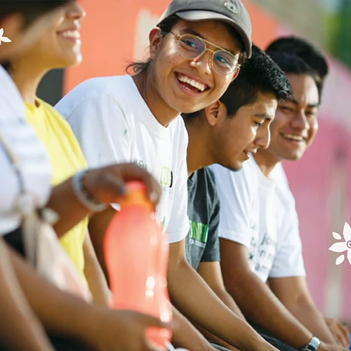 a young person in glasses sitting with friends along a wall