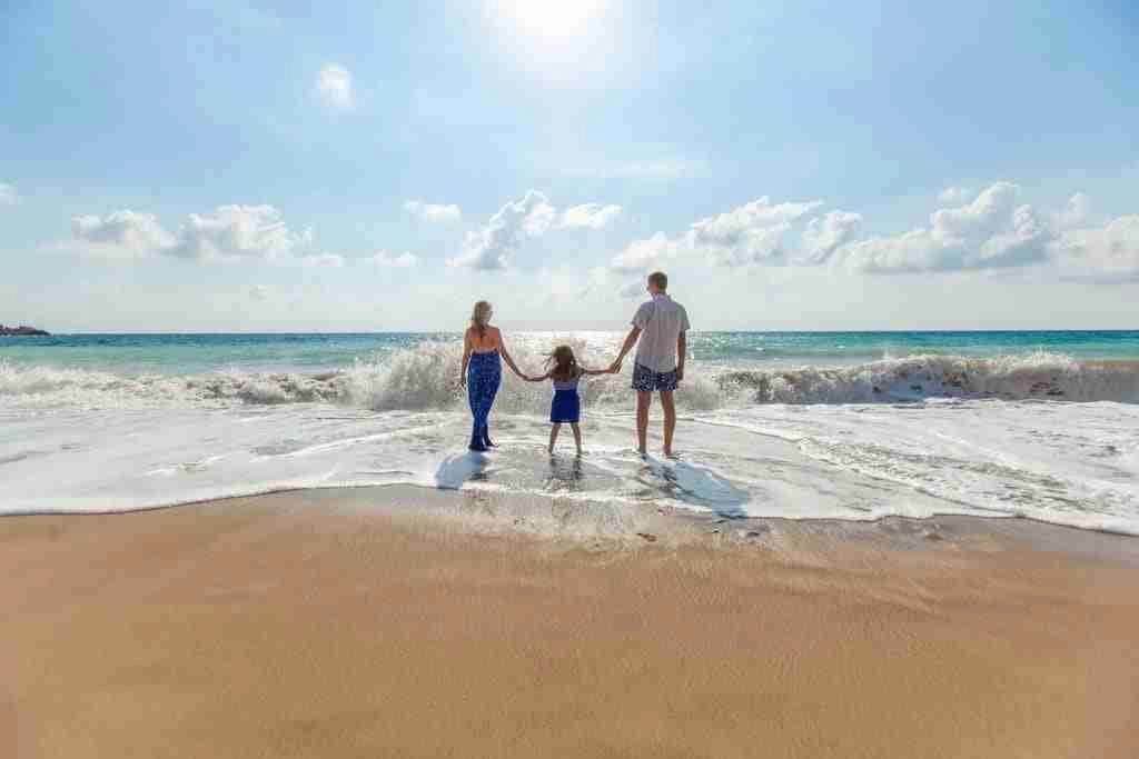 A woman, young girl and man holding hands walking in the waves at the beach