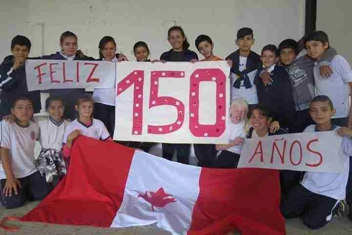 Group of children holding a candaian flag and banners to show their support for Canada Day in Paraguay